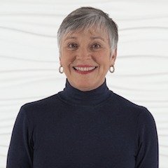 A smiling person with short gray hair wearing a navy turtleneck, representing healthcare training for Medbridge.