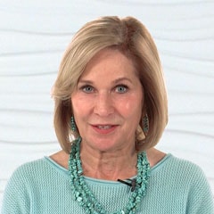 A woman with short blonde hair wearing a turquoise sweater and necklace stands in front of a white background for medbridge.