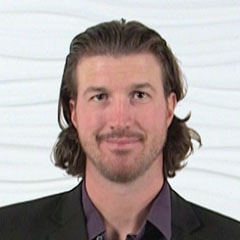 A man with brown hair and a beard in a dark blazer represents medbridge's innovative hybrid care solutions.