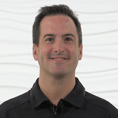 A person with short dark hair smiles in a black collared shirt, conveying professionalism for medbridge hybrid care training.