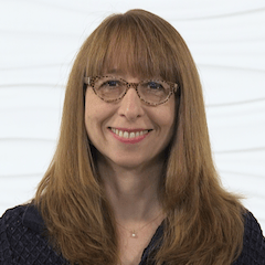 A smiling person with long brown hair and glasses, wearing a dark patterned top, symbolizes digital healthcare education for medbridge.