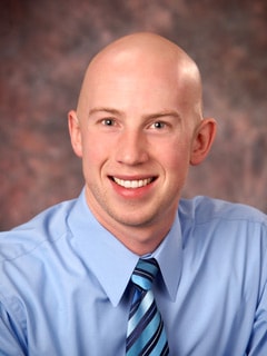 A smiling man in a blue shirt and striped tie poses against a blurred brown background, representing the future of digital healthcare at medbridge.