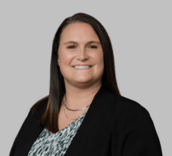 A smiling individual in a black blazer and patterned top represents digital healthcare, against a gray backdrop, for medbridge.