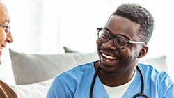 Home health clinician smiling and speaking with an older adult patient, representing patient satisfaction in home health care.