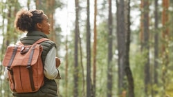 Individual with a backpack in a forest looking sideways at tall trees.