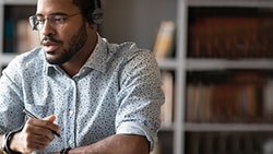 A man with headphones at a desk uses a laptop, representing Medbridge.