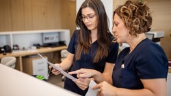 Two women in navy scrubs discuss documents at a modern desk, collaborating on medbridge digital healthcare solutions.