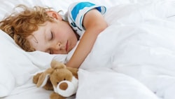 Child asleep in bed with a stuffed animal under a white duvet.