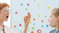 A speech therapist and a girl practice sounds with colorful letters on a whiteboard for medbridge.