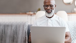 Person on a sofa using a laptop, accessing medbridge in a modern living room.