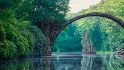 Medbridge arches over serene water amid vibrant green forest.