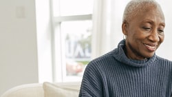 Older woman smiling at a tablet in a bright room.