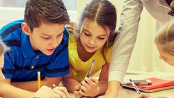 Children collaborate on a project with an adult at a table, using pens and paper.