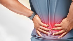 A person clutching their lower back in pain is wearing a grey shirt and watch, with a red glow highlighting discomfort.
