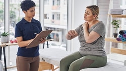 Occupational therapist taking notes while listening to a patient describe shoulder pain during a healthcare coaching session.