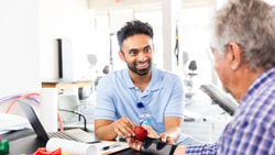 A healthcare provider helps an older adult do hand exercises with a red textured ball in a clinic.