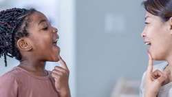 A child and adult practice speech by pointing to their open mouths.