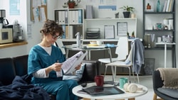 Healthcare professional in scrubs reviewing patient records in a breakroom, related to habilitative vs. rehabilitative billing.