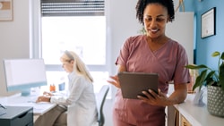 A healthcare worker in scrubs uses a tablet as another in a white coat works at a desk, showing medbridge digital health.