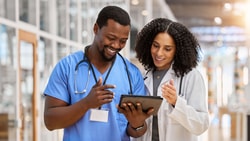 Two healthcare professionals reviewing a digital tablet in a hospital setting, discussing Bundled Payments for Care Improvement (BPCI).