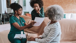 Nurse discussing care plan with an older adult and family member at home, highlighting caregiver burden in rehabilitation settings.