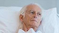 Elderly man with nasal cannula in hospital bed, looking sideways.