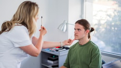 Clinician performing an oculomotor test to assess central vs. peripheral vestibular dysfunction in a seated patient.