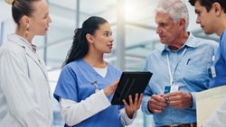 Hospital care team in scrubs and lab coats reviewing patient outcomes on a tablet during a discharge planning discussion