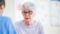 An elderly woman with glasses talking to a medbridge healthcare worker.