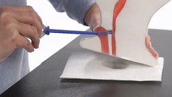 A person uses a blue applicator to fix a broken white object with red accents on a black surface.