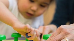 A child plays with a pegboard toy as an adult provides guidance.