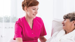 A nurse in pink chats with an elderly patient in bed at Medbridge.