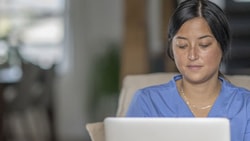 Individual in a blue shirt using a laptop on a beige couch, Medbridge setting.