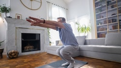 Older adult performing a squat exercise at home for fall prevention, improving strength and balance through evidence-based training.