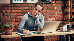 Athletic trainer studying CEU requirements on a laptop and taking notes to prepare for the certification renewal deadline.
