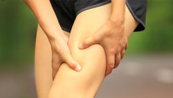 Person clutching their thigh on a blurry outdoor path, suggesting injury.