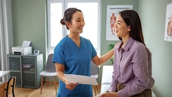 Nurse supporting patient while reviewing the head-to-toe assessment checklist in a clinical exam room.