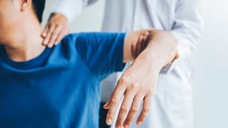 Physical therapist assisting a patient’s shoulder as part of a referral assessment.