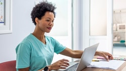 A person in scrubs reviews paperwork on a laptop at a medbridge office desk.