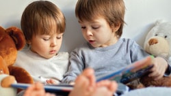 Two kids with stuffed bears read a book together.