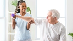 A healthcare provider helps an older man lift a dumbbell, illustrating hybrid care with medbridge.