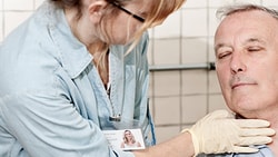 A medbridge healthcare worker checks the pulse of a calm older man in light blue attire.