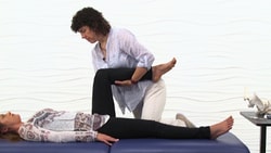 A physical therapist bends a patient's knee with medbridge equipment nearby.