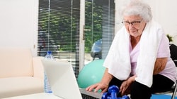 Elderly woman with a towel using a laptop in a bright room, with a dumbbell nearby, on medbridge platform.