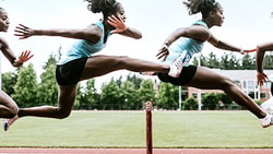 An athlete in sportswear leaps over a hurdle on a track.