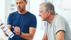A man in a blue shirt presents a tablet to an older man in a gray shirt inside, showcasing medbridge.