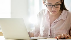 A person using a laptop at a desk with medbridge materials and a small plant.