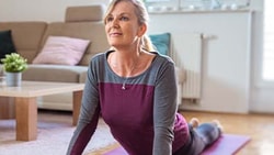 A woman practices cobra pose on a yoga mat in a living room.