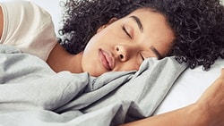 Woman peacefully sleeping in bed with soft lighting, representing sleep hygiene and restorative rest strategies.