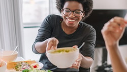 Two people enjoying a meal with fruits and salads in a bright room, one holding a bowl.